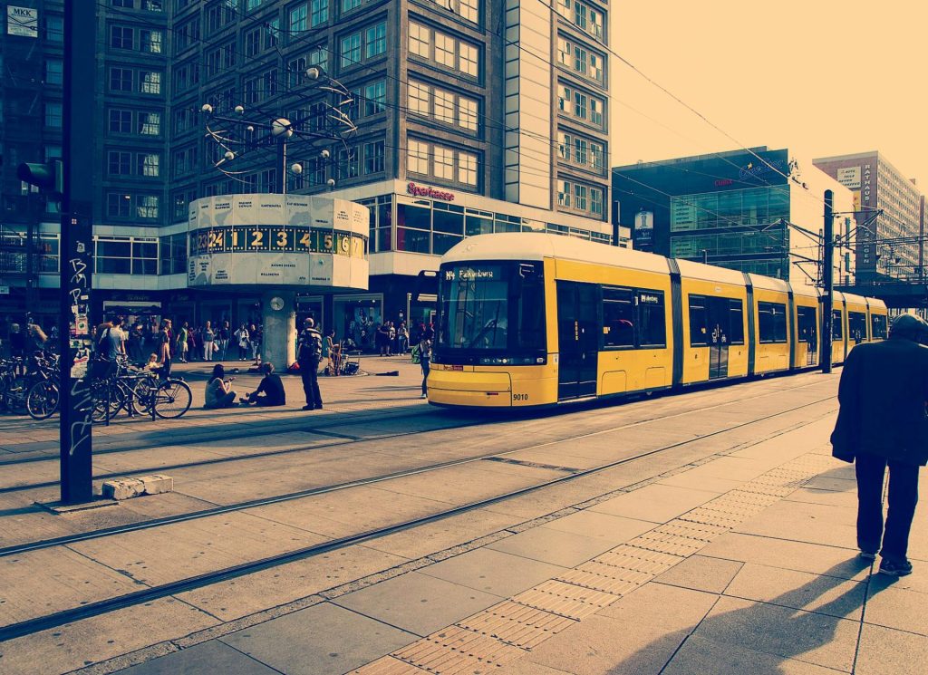 Lebhaftes Stadtbild in Berlin mit einer gelben Straßenbahn und Menschen auf dem Alexanderplatz.